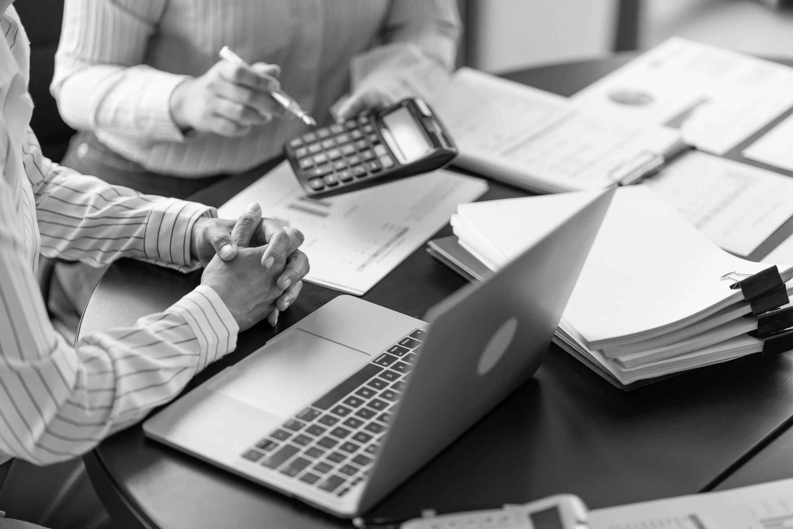 Two people analyzing financial documents with a calculator and laptop.
