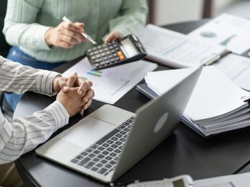 Two people analyzing financial documents with a calculator and laptop.