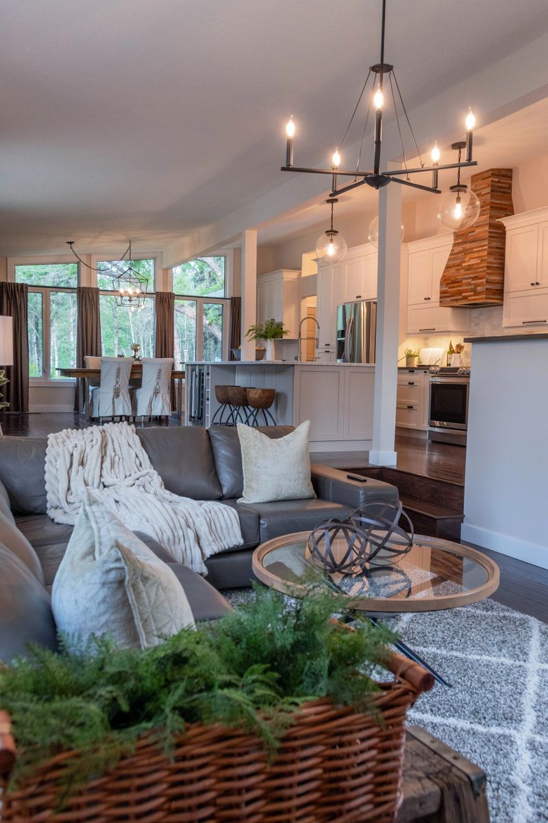 Leather couch with pillows and cozy blanket in sunken living room looking into a modern country style open concept kitchen with rustic wooden hood fan and huge quartz island for entertaining.