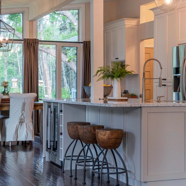 Modern kitchen with wooden stools and large windows overlooking greenery.