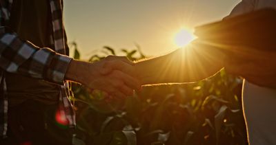 Two farmers shaking hands with a crop in the background