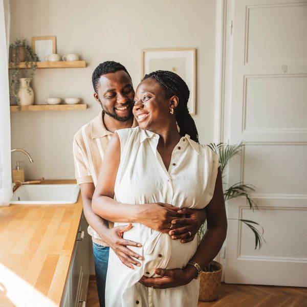 Happy couple embracing with woman showing pregnancy in a sunlit kitchen.