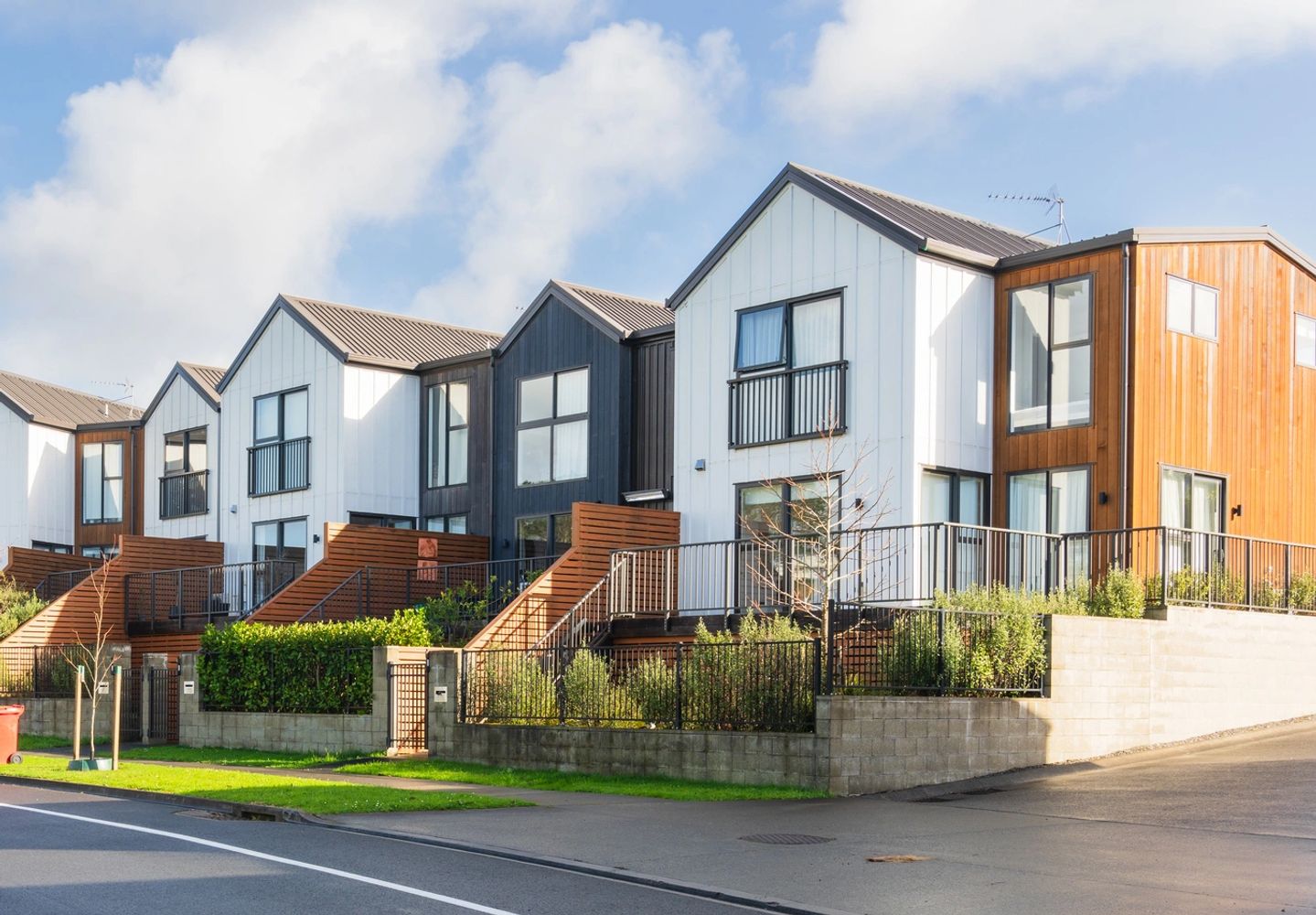 Modern townhouses with wood and white paneling along a curved street.