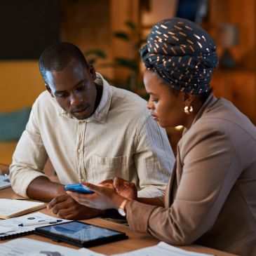 Two people discussing work with documents and devices on table.