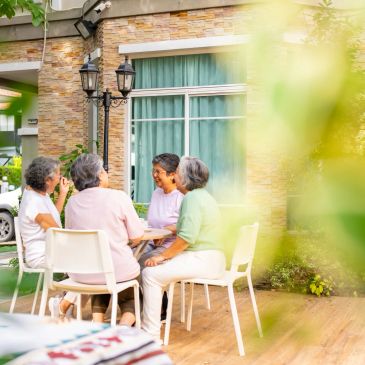 Four elderly women chatting outdoors on a porch.