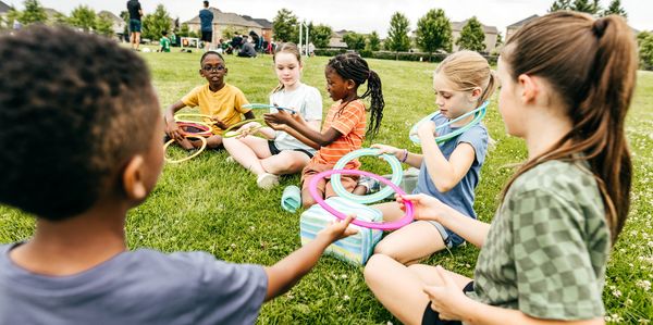 Children sitting on grass, playing with colorful rings outdoors.