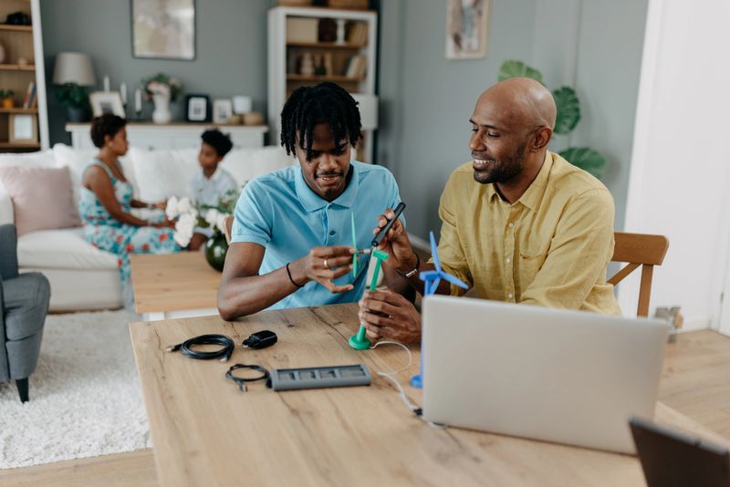 A father and son duo collaborates in assembling wind turbine models, symbolizing their mutual interest in sustainable technology and shared educational journey within a home setting.
