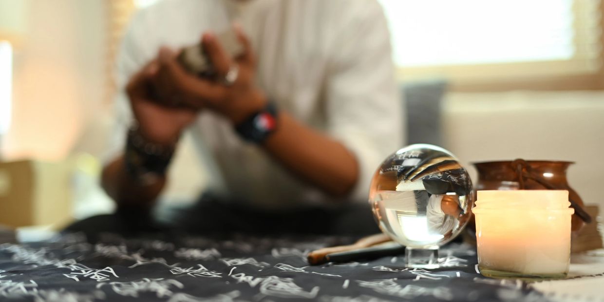 A person holds cards with a candle and crystal ball on a table.