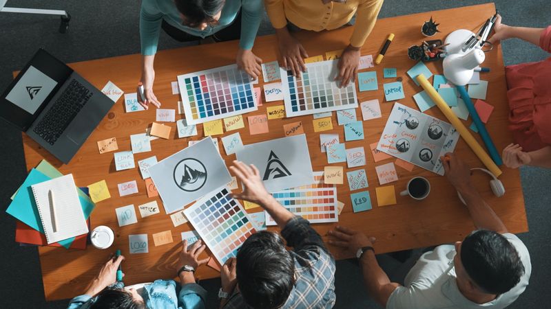Top view of business team write graphic logo on meeting table with colorful sticky notes and design while explain idea. Project manager sharing idea and explain concept art to smart team. Symposium.