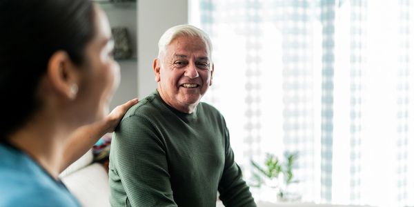 A caregiver comforting a smiling elderly man in a bright room.