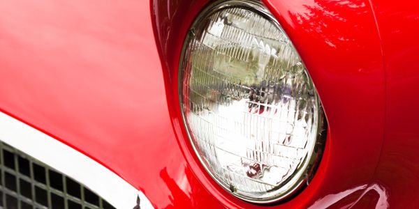 Close-up of a shiny red vintage car headlight and grille.