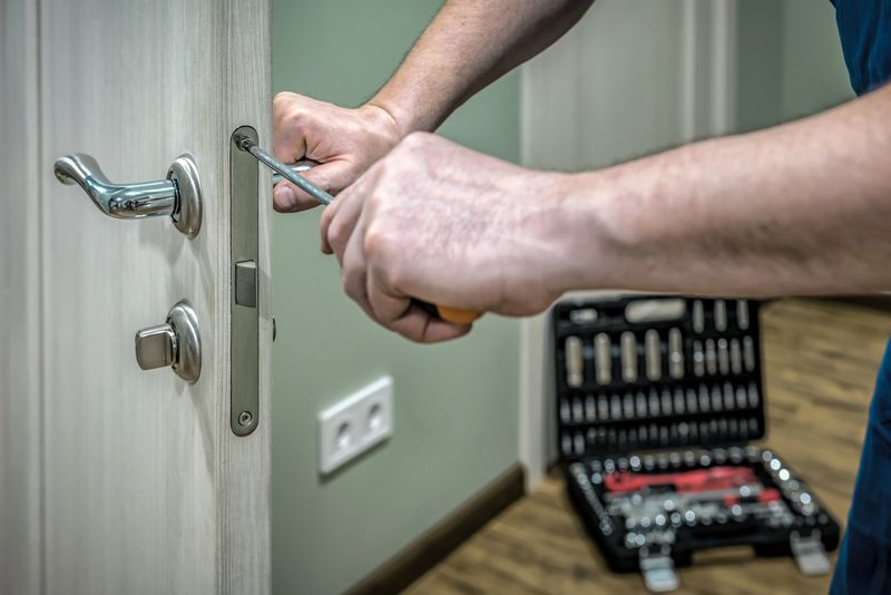 Professional locksmith worker installing, working with house door lock using screwdriver. Industrial theme