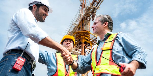 Construction workers shaking hands at a site with crane in background.