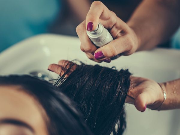 A person spraying liquid onto wet hair over a sink.