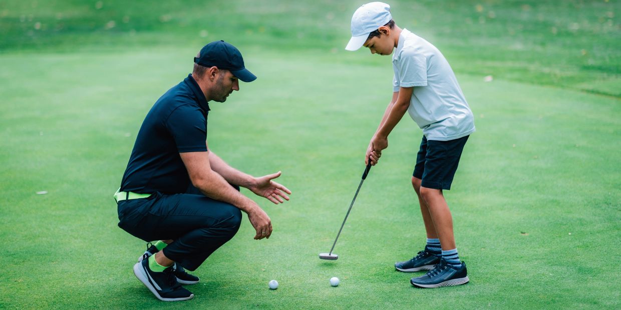 A man coaching a boy in golf putting on a green.