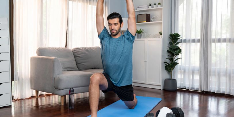 Man on blue yoga mat at home with dumbells on the floor next to the yoga mat. 