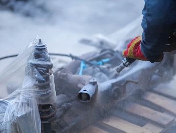 Person spray painting metal parts outdoors.