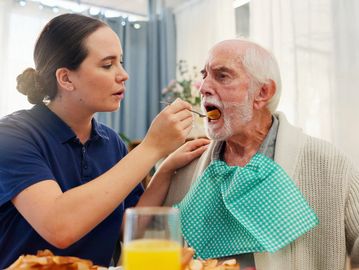 Woman feeding elderly man with a spoon.