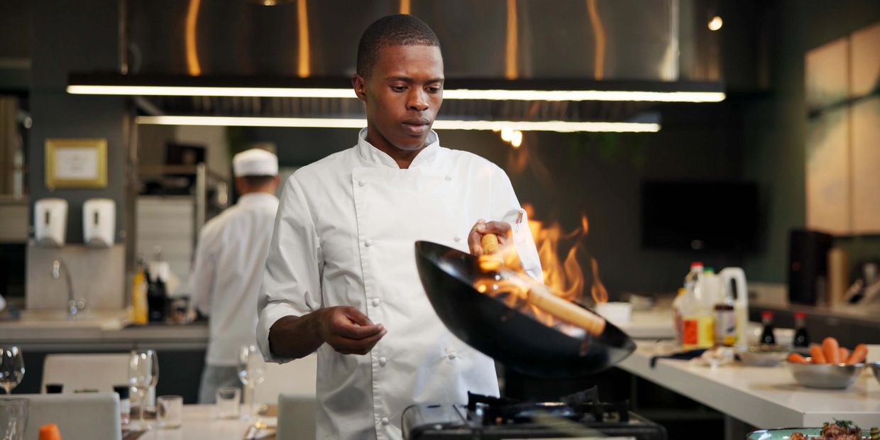 Restaurant chef cooking with a wok in a clean and well-ventillated kitchen