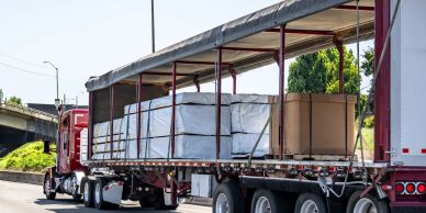A semi-truck with an open trailer carrying large wrapped cargo.