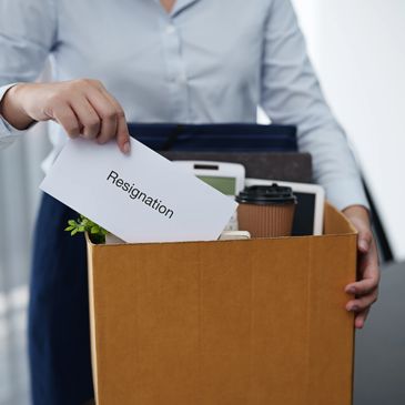 Person placing resignation letter in box filled with personal items.