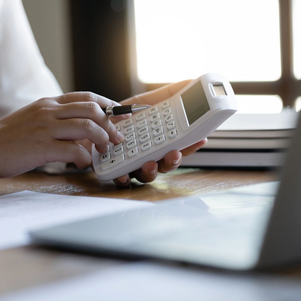 Person using a white calculator, holding a pen.