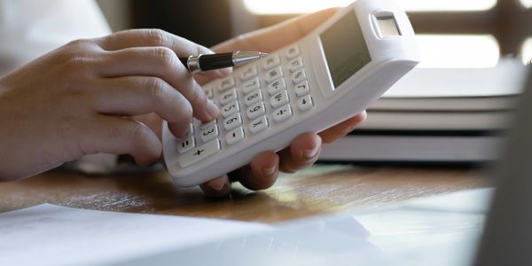 Person using a white calculator, holding a pen.
