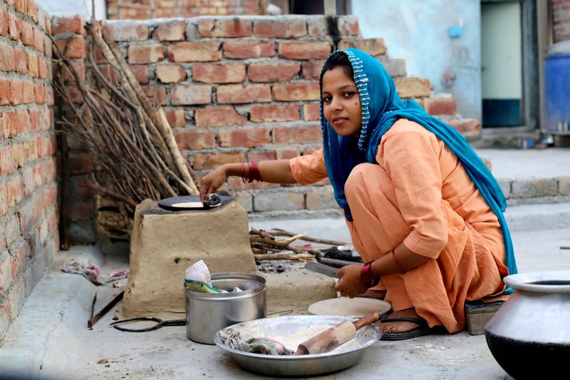 Cheerful women of Indian ethnicity cooking food on mud stove at home sitting portrait close up.