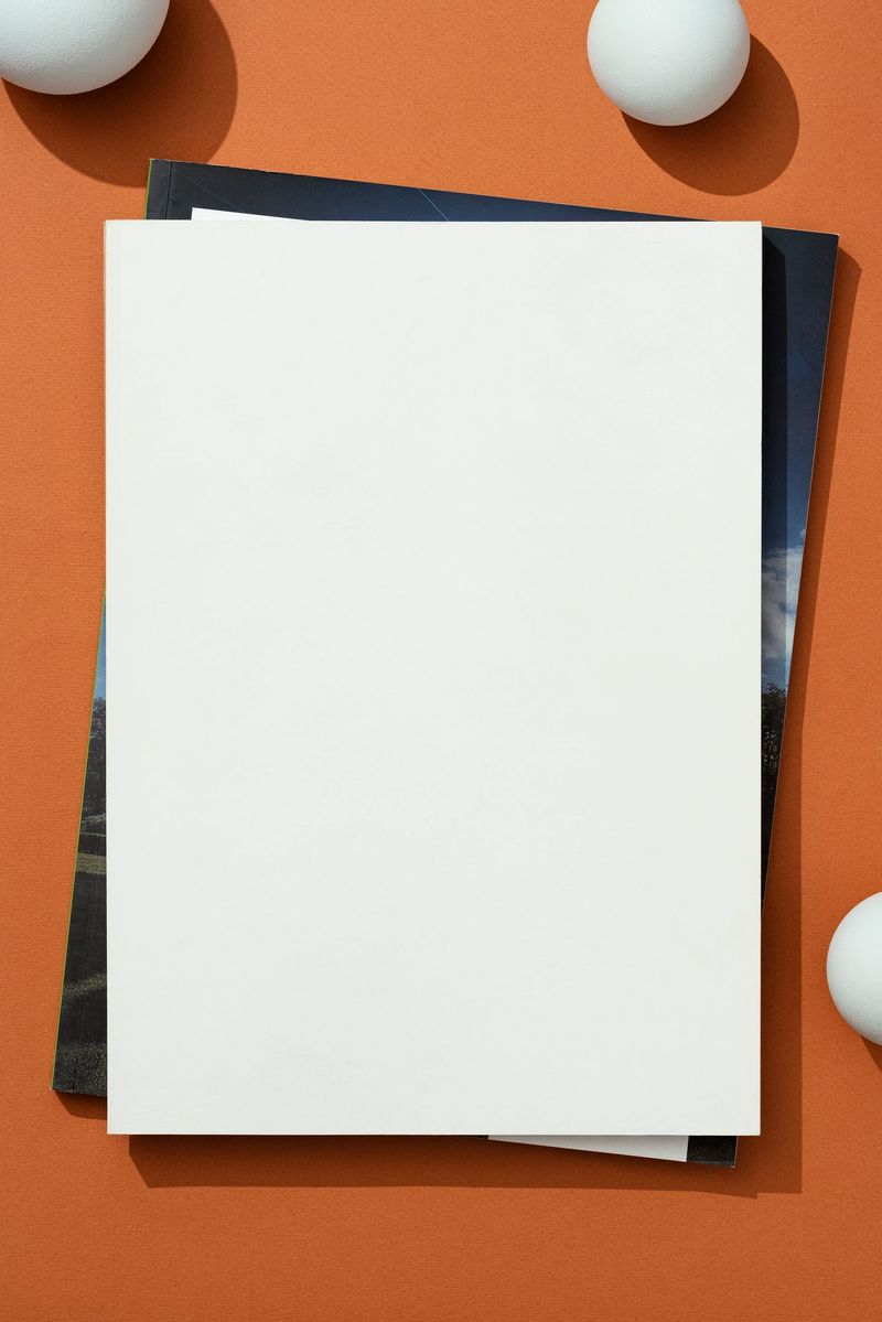 Still life of directly above table top shot of white blank magazine cover mockup on orange background