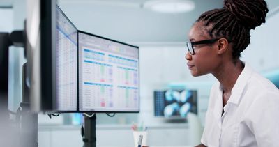 A female scientist analyzing data on dual monitors in a lab.
