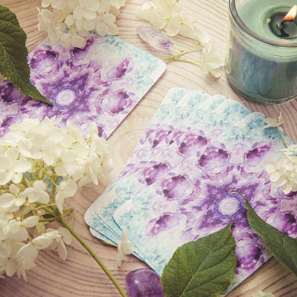Tarot cards, white flowers, and a lit candle on a wooden surface.