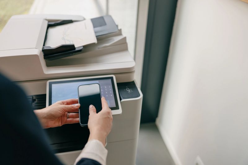 Person using a smartphone to operate a modern printer in an office setting, showing tech integration