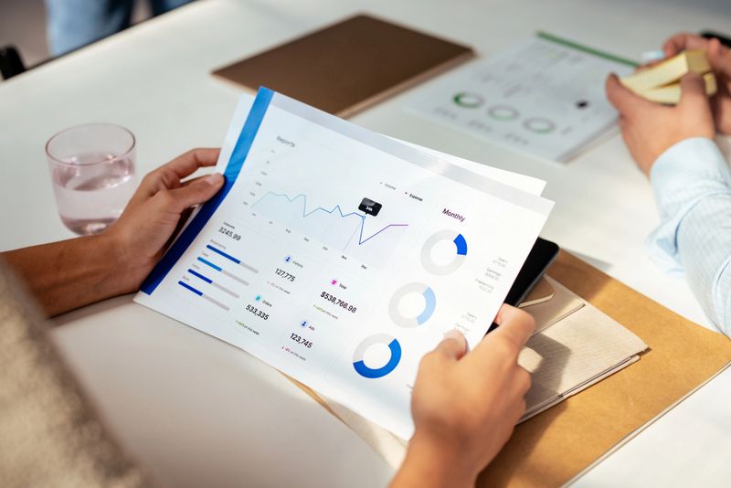 Close-up of hands holding financial documents with graphs and charts during a business meeting. Professionals discussing data analysis.