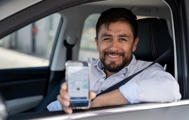 Man smiling in car showing phone with app.