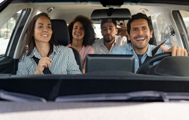 Happy group of Latin American friends going on a road trip and dancing in the car