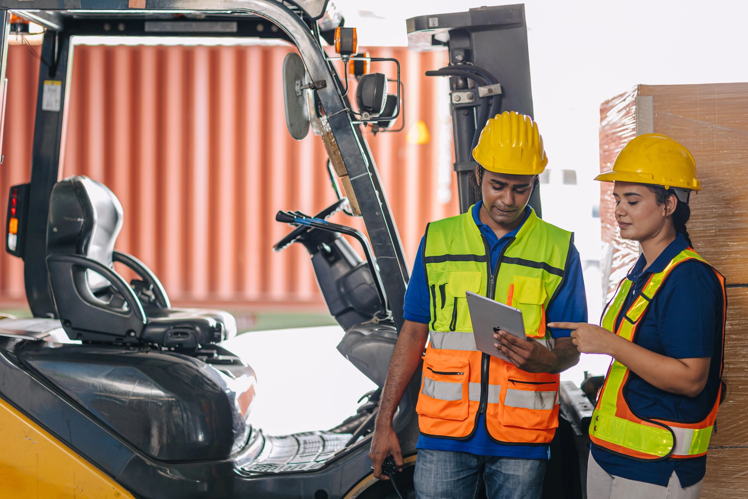 Two warehouse workers reviewing a tablet near a forklift.