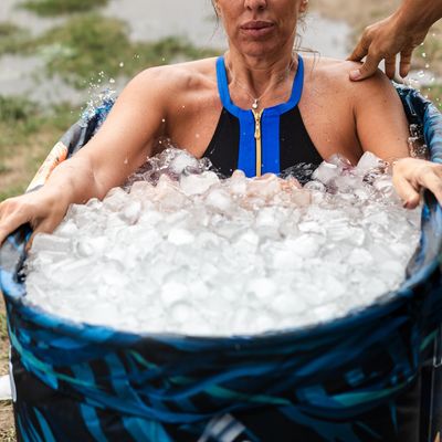 Woman in a wetsuit sitting in a tub filled with ice water outdoors.