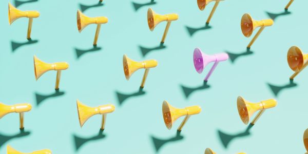 A single pink megaphone among many yellow megaphones on a blue background.