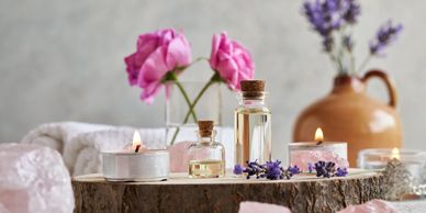 Aromatherapy setup with candles, essential oils, pink roses, and lavender on a wooden slab.