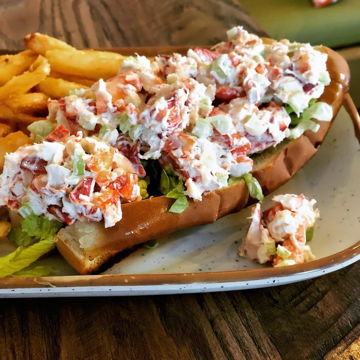 Lobster roll sandwich with lettuce and a side of fries on a plate.