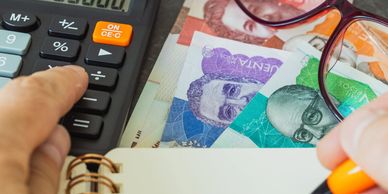 Mano usando calculadora con billetes y libreta.