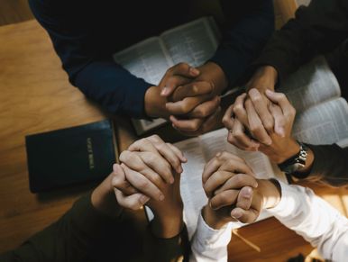 People holding hands and praying over an open Bible.