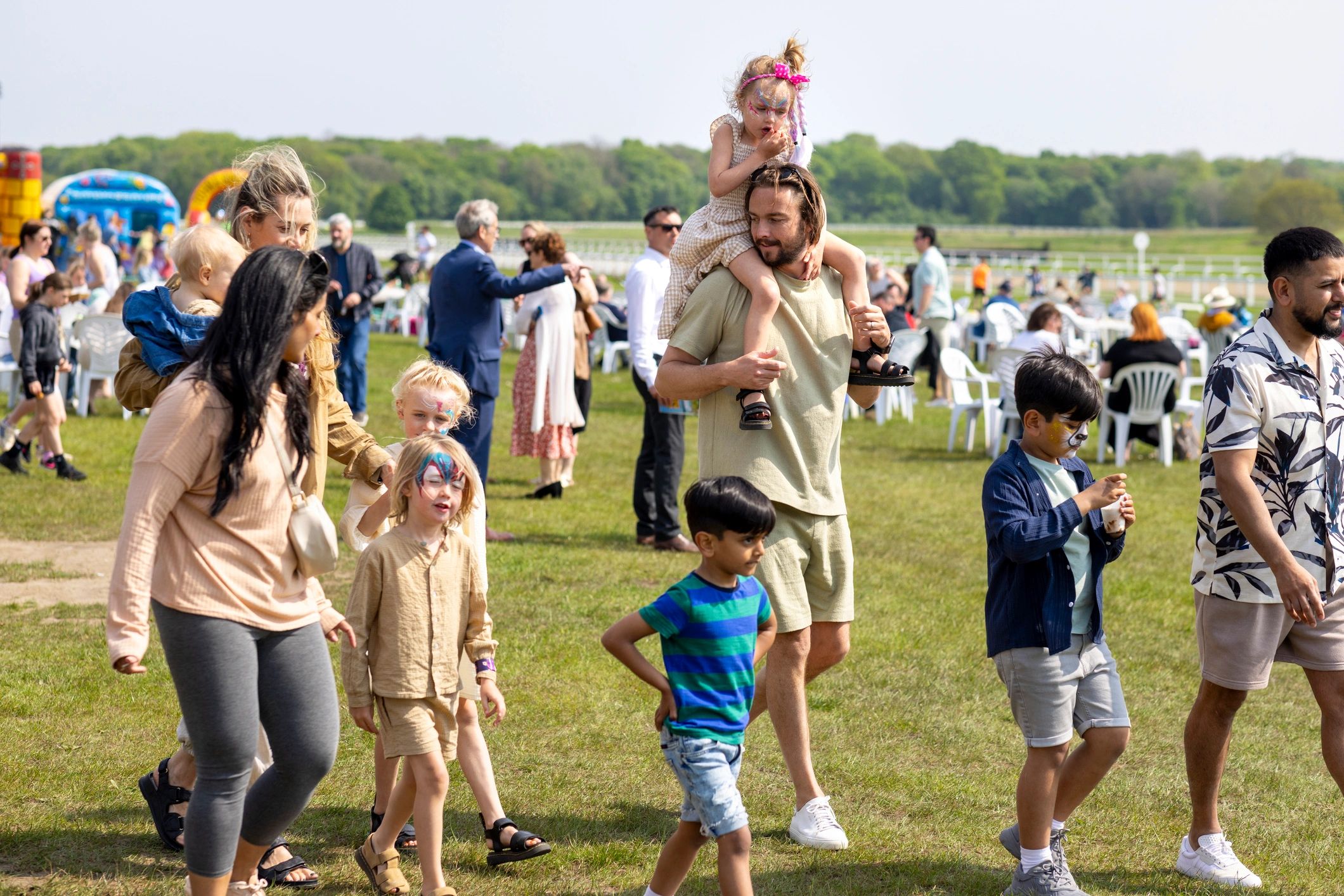 Families enjoying a sunny day at an outdoor festival with face painting and activities.
