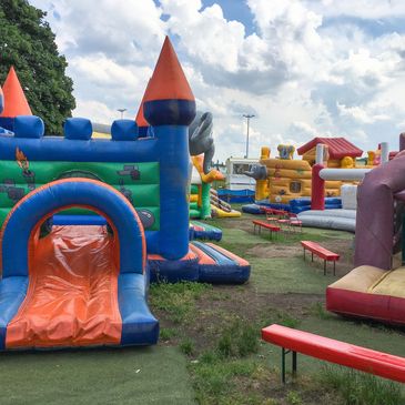 Inflatable bounce houses and slides set up in an outdoor play area under a cloudy sky.