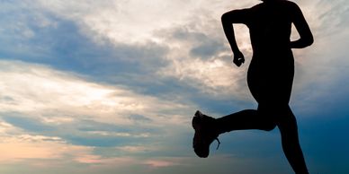 Silhouette of a person running against a cloudy sky at dusk.