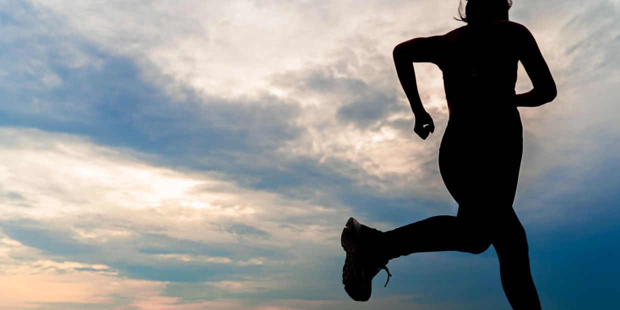 Silhouette of a person running against a cloudy sky at sunset.