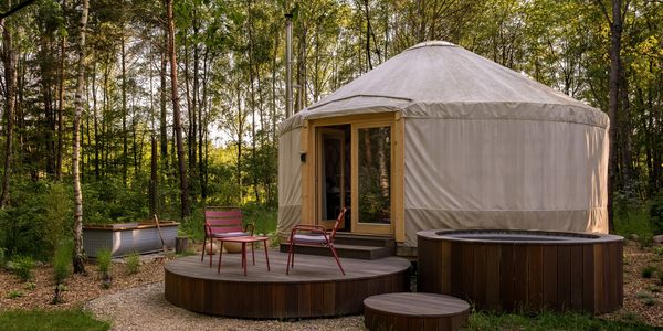 A cozy yurt with wooden deck and red chairs in a lush forest setting.