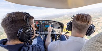 Two pilots flying a small aircraft, one pointing at the controls.