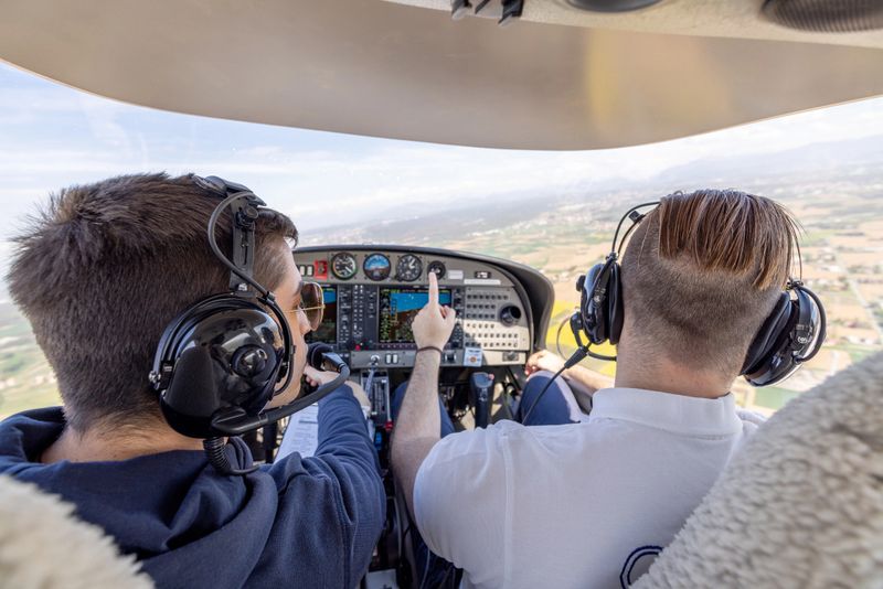 Two pilots in the cockpit of a small aircraft, wearing headsets, discussing navigation and controls. The cockpit displays various instruments, and the view outside shows a scenic landscape.