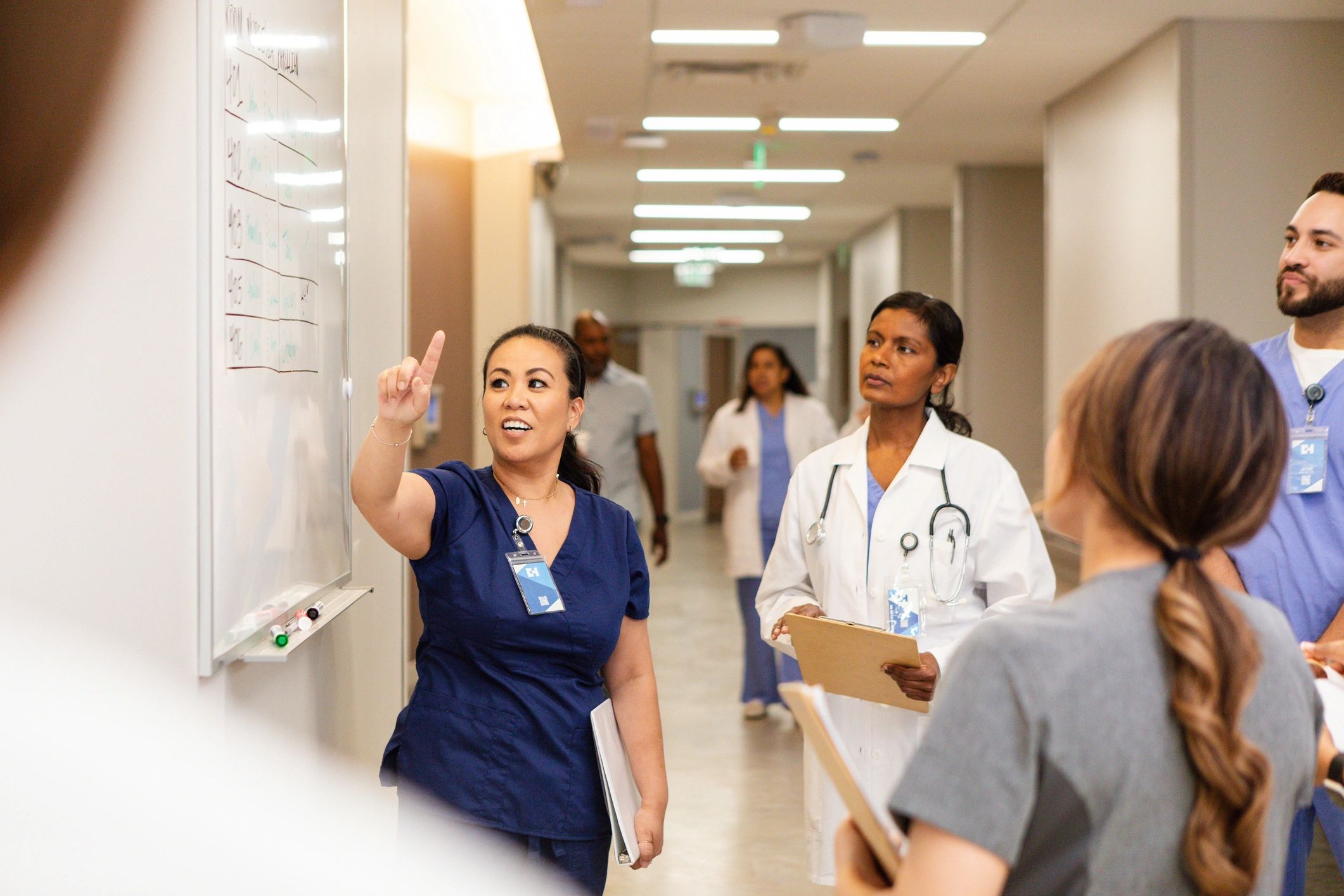 Healthcare professionals discuss patient information on a whiteboard in a hospital hallway.